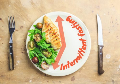 Intermittent fastin concept. One-third plate with healthy food and two-third plate is empty. Chicken fillet, arugula and tomatoes on a plate. Top view. Flat lay