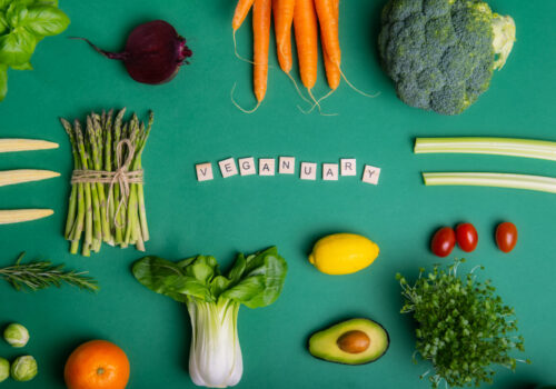 Top view set of healthy raw vegetables on the green background with Veganuary message on wooden blocks. Vegetarian and vegan diet. Veganism concept. Sustainable lifestyle, good, real plant-based foods.